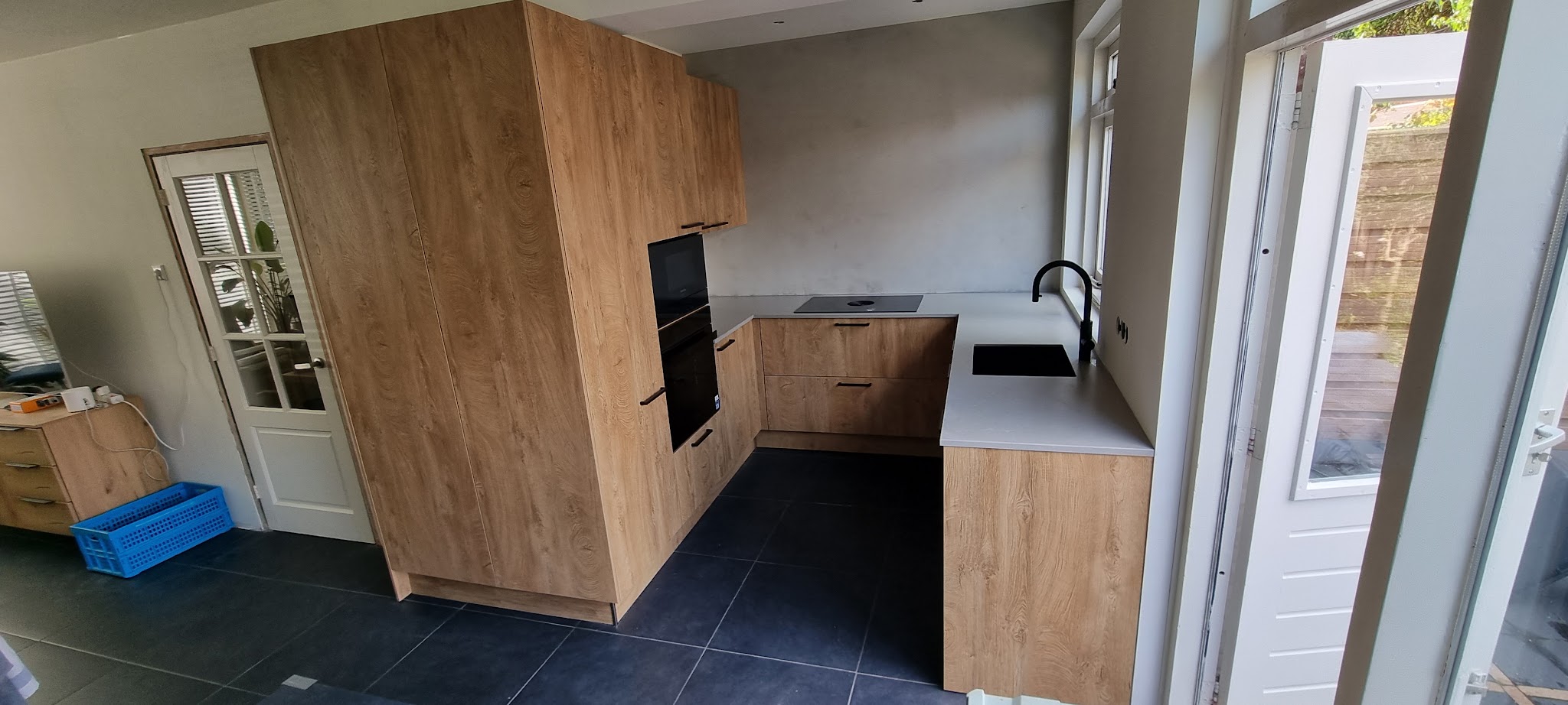 Keuken met eikenhouten hoge kasten, wit werkblad en zwarte kraan